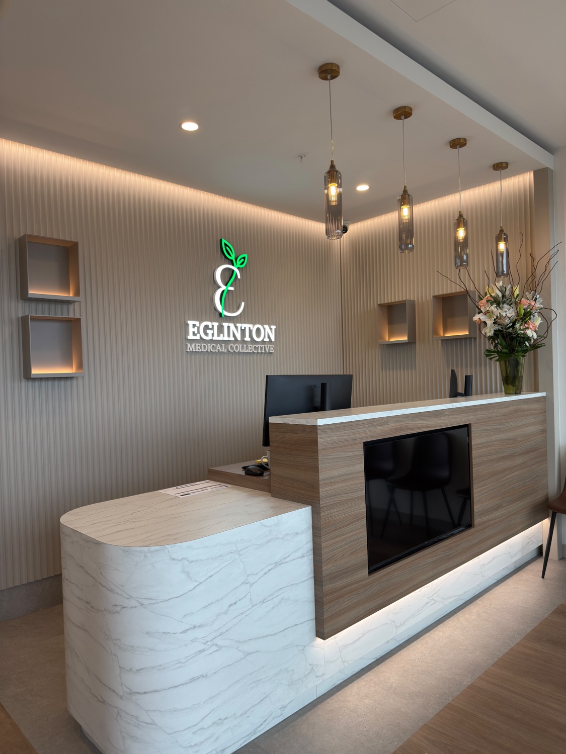 The reception desk at Eglinton Medical Collective, with its illuminated logo and marble counter